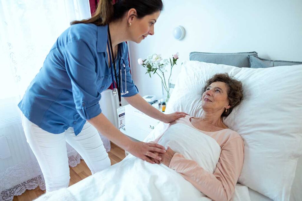 An older adult unpacks a box of personal items in a cozy, light-filled bedroom.